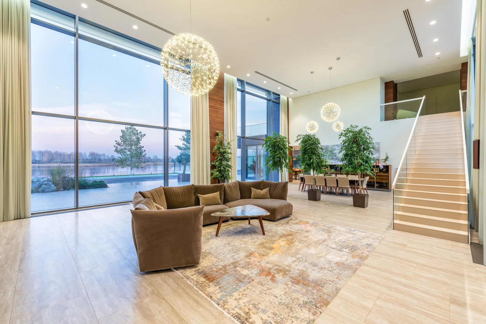 Light-filled contemporary living room with double-height glass, pale blue lake views and a white staircase